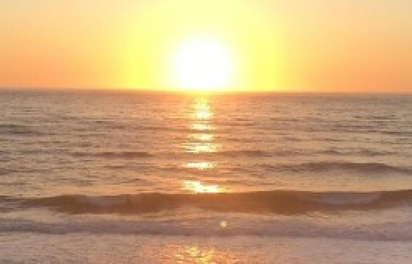 image of sun setting behind the ocean with golden sky